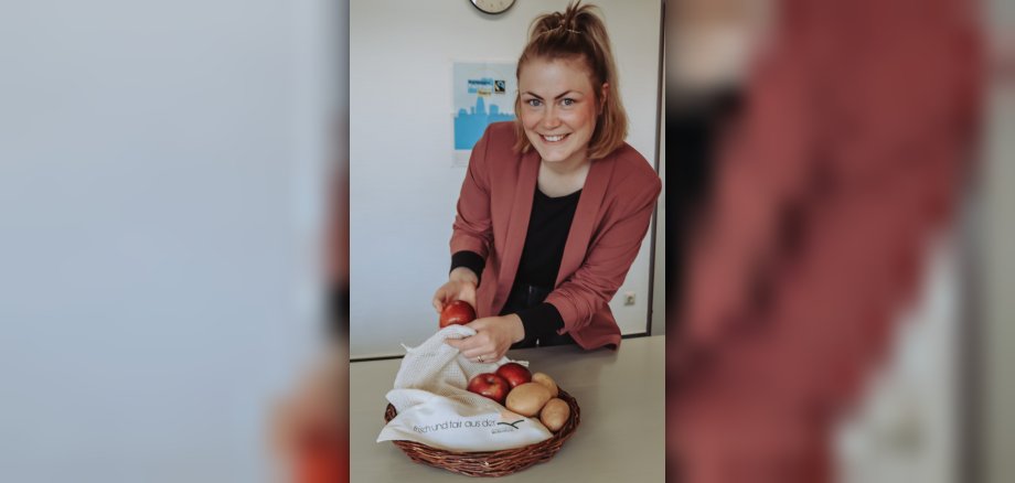 Projektbeauftragte Kim Lachmann zeigt  Obstbeutel aus fair gehandeltem Material und packt Äpfel hinein. 