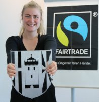 VG wird Fairbandsgemeinde Projektbeauftragte Kim Lachmann zeigt das Wappen der Verbandsgemeinde Weißenthurm, im Hintergrund hängt ein Plakat mit dem Fairtrade-Logo an der Wand.