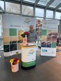 Fairer Valentinstag VG-Mitarbeiterin Ulrike Rieden steht an einem Info-Stand mit fairen Rosen und Info-Material im Foyer des VG-Rathauses.