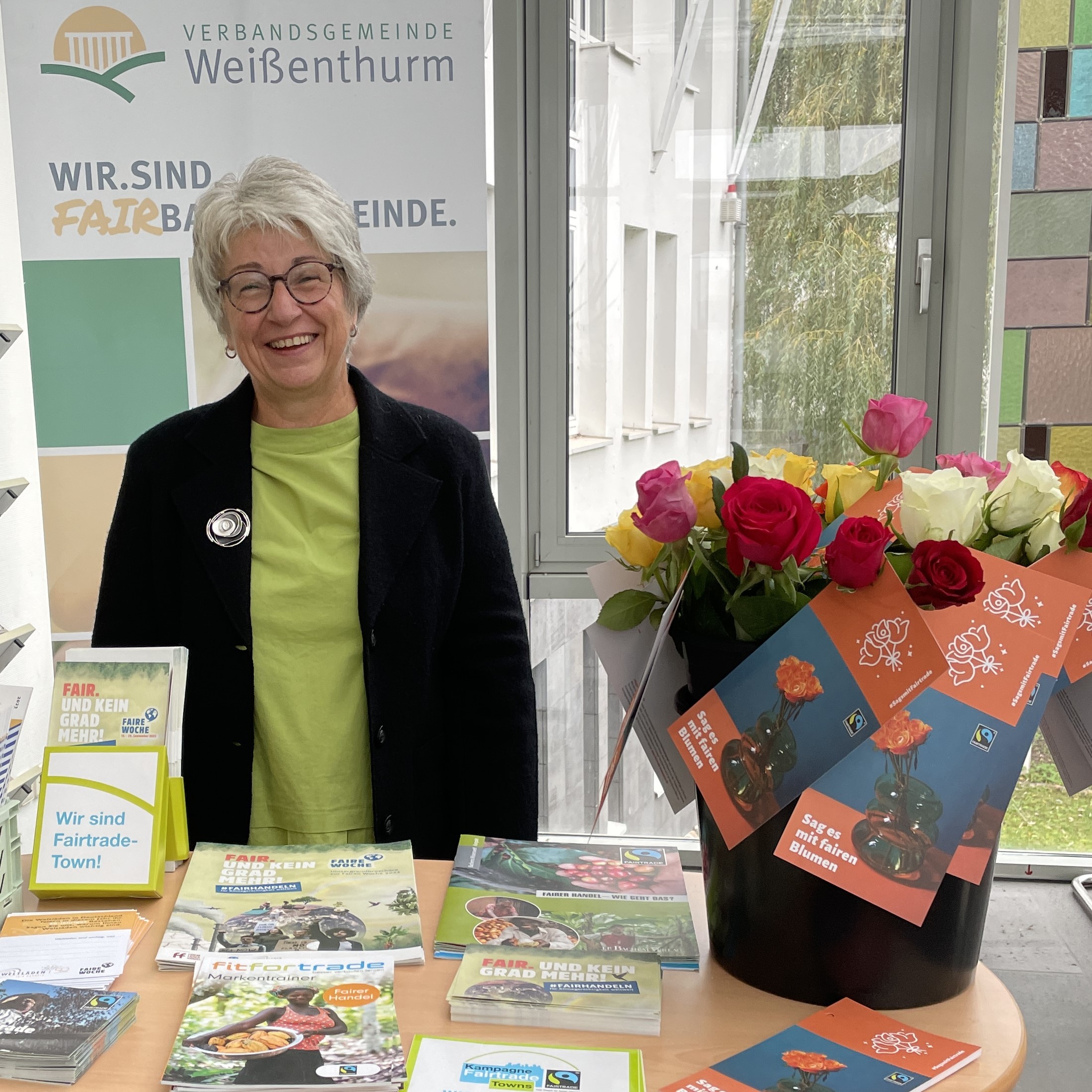 Gaby Kohns steht an einem Fairtrade-Stand mit Rosen und Info-Material im Foyer des VG-Rathauses.