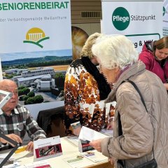 Am Stand des Seniorenbeirates informiert sich eine weißhaarige, ältere Dame bei einem Mitglied des Seniorenbeirates. Im Hintergrund steht ein Rollup des Seniorenbeirates. 