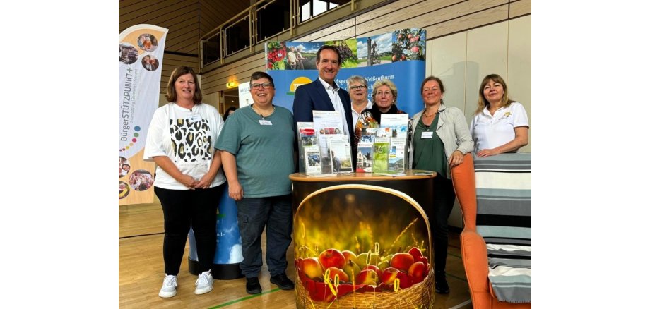 Am Touristik-Stand der VG Weißenthurm mit einem Korb Äpfel vorne steht in der Mitte Bürgermeister Przybylla mit den Organisatorinnen.