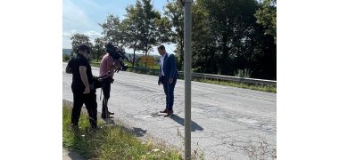 Auf der Straße steht Bürgermeister Przybylla und zeigt dem links stehenden Drehteam die Schlaglöcher.