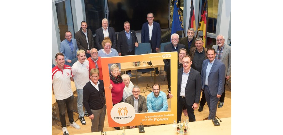 Von oben fotografiert sind die Vertreter der Vereine, die gefördert werden, die Vertreter der evm und der VG zu sehen, zum Teil durch einen orangefarbenen Rahmen mit evm-Logo.