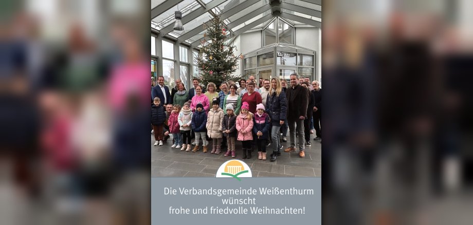 Bürgermeister Thomas Przybylla steht mit Mitarbeiterinnen und Mitarbeitern der VG und Kita-Kindern vor dem geschmückten Weihnachtsbaum. 