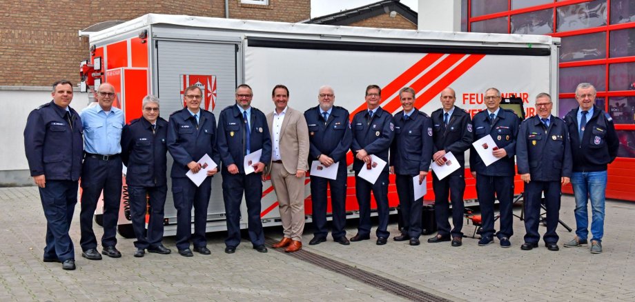 Vor dem Feuerwehrgerätehaus und einem Löschfahrzeug stehen alle Geehrten mit Bürgermeister Thomas Przybylla und Wehrleiter Arnd Lenarz. 