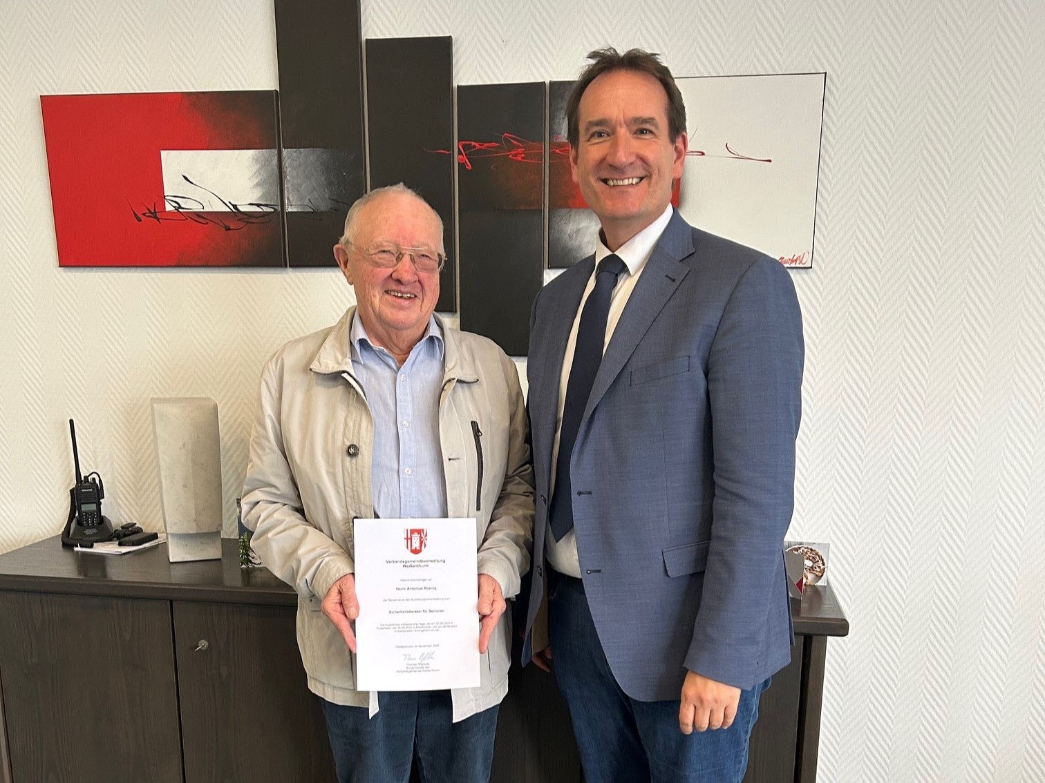 Antonius Rüsing steht links von Bürgermeister Thomas Przybylla vor einem Sideboard und hält seine Ernennungsurkunde in der Hand.