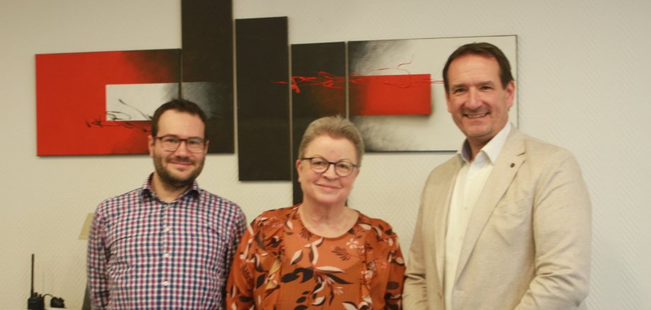Personalratsmitglied Christian Volk, Diethild Eßer und Bürgermeister Thomas Przybylla vor einem rot, grau, weißen Bild