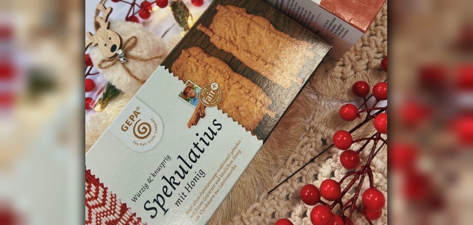 Faire Weihnachtswoche Eine Schachtel fair gehandelter Spekulatius liegt neben roten Beeren und weihnachtlicher Deko.