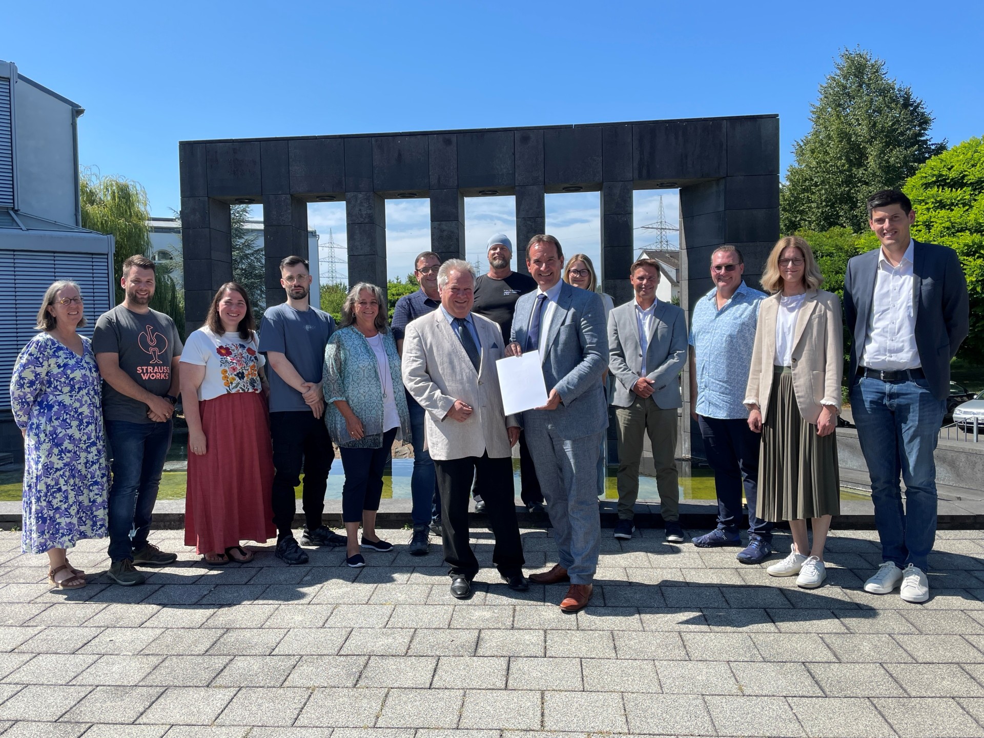 Abschied Pohling Gruppe Der scheidende Personalratsvorsitzende Holger Pohling steht vor dem Rathaus neben Bürgermeister Thomas Przybylla, der die Dankesurkunde in der Hand hält, dahinter weitere Kolleginnen und Kollegen.