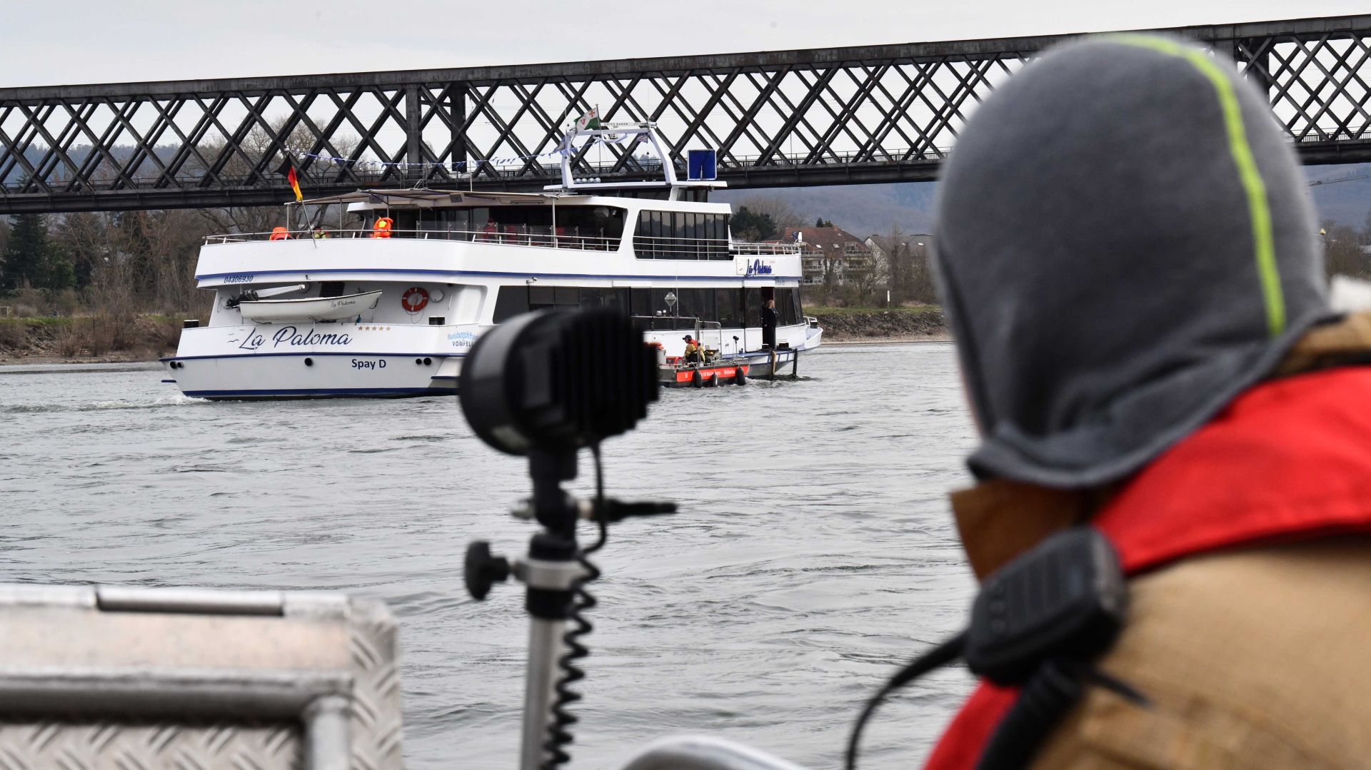 Feuerwehr-Übung Fahrgastschiff Von einem Feuerwehrboot mit einem Feuerwehrmann im Vordergrund am rechten Bildrand ist das havarierte Schiff und die Eisenbahnbrücke zu sehen.