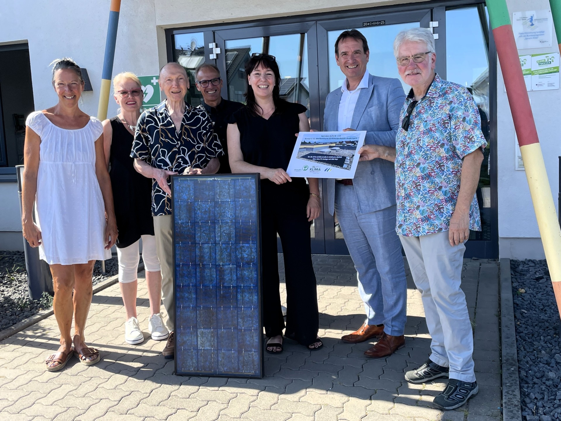 Balkonkraftwerk Kita Schillerstraße Vor dem Eingang der Kita Schillerstraße stehen Bürgermeister Thomas Przybylla mit der Kita-Leiterin Kirsten Zimmer und Vertreterinnen und Vertretern der Klimafit-Gruppe, die ein Solarmodul und ein kleines Plakat in der Hand halten.
