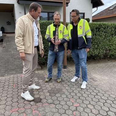 Breitbandausbau in der VG Weißenthurm Bürgermeister Thomas Przybylla steht mit den beiden VG-Mitarbeitern Reinhold Jeck und Joachim Freund an einer Stelle der Straße, auf der rote Markierungen zu sehen sind.