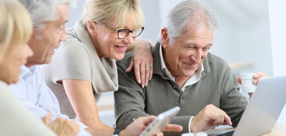 Eine Gruppe von Seniorinnen und Senioren sitzt an einem Laptop. 