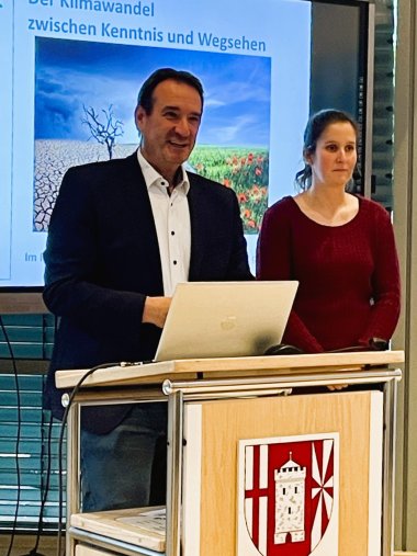 Vortrag Klimawandel Referentin und Bürgermeister Bürgermeister Thomas Przybylla steht mit der Klimaschutzmanagerin Jennifer Vogt am Rednerpult, dahinter ein Bildschirm mit der Präsentation der Referentin.