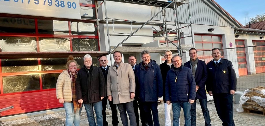 Bürgermeister Thomas Przybylla steht mit WehrleiterArnd Lenarz, dem Bassenheimer Wehrführer Michael Röser und Mitgliedern des Ältestensrates vor dem eingerüsteten Anbau an das Feuerwehrgerätehaus. 