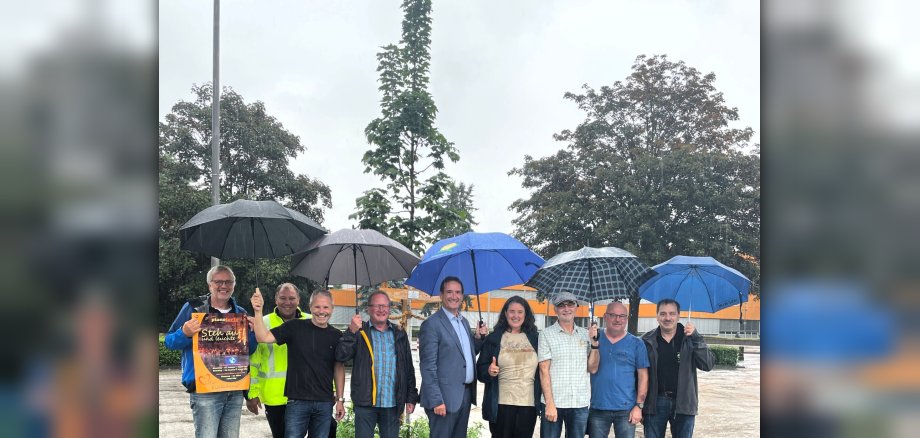 Unter Regenschirmen stehen vor einem neu gepflanzten Baum Bürgermeister Przybylla, Vertreter der ÖK-Gruppe, des Chores Piano Forte und der anderen, an der Pflanzaktion beteiligten Firmen.