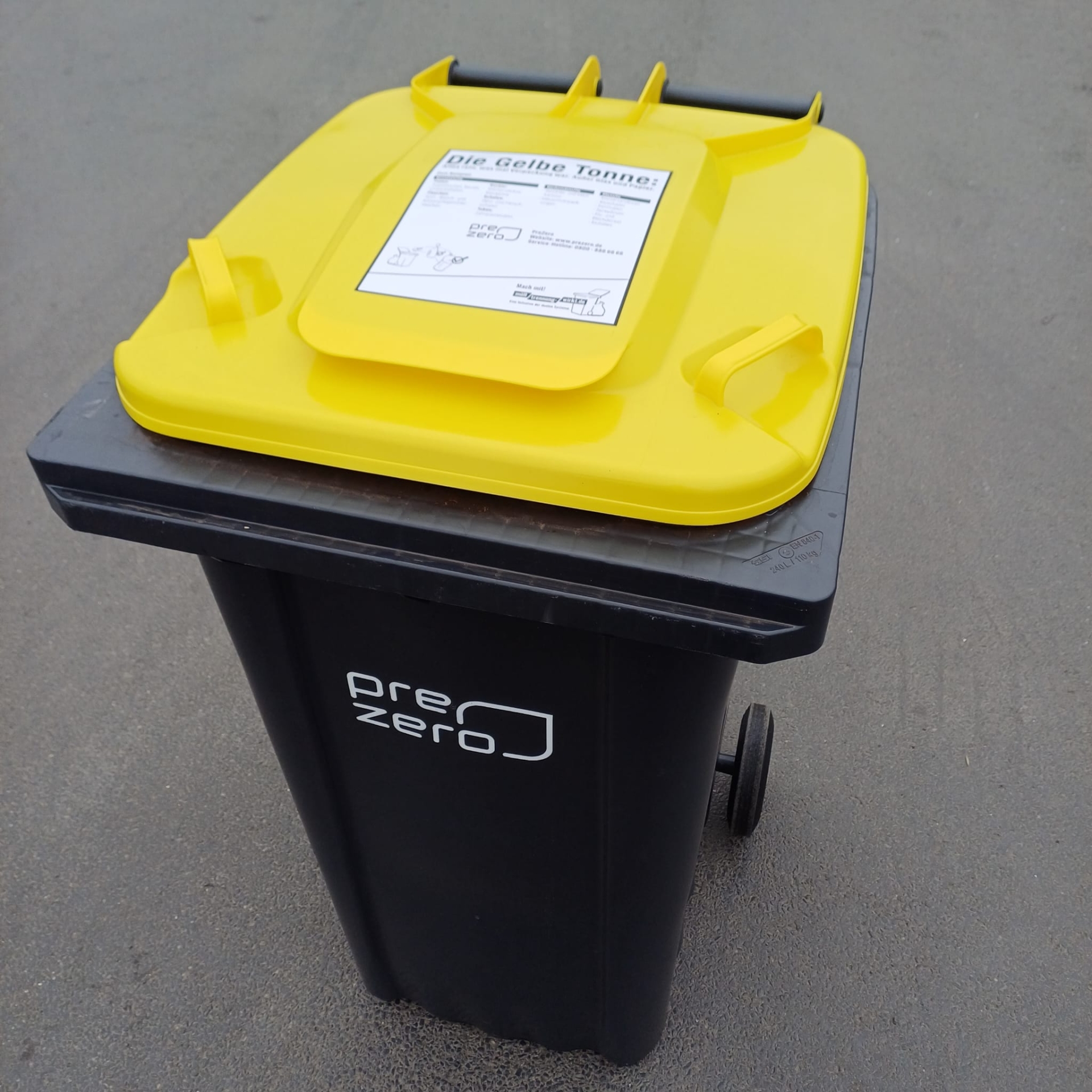 Gelbe Tonne mit Aufkleber Auf dem gelben Deckel einer schwarzen Mülltonne klebt ein Info-Hinweis zur Befüllung des Behälters.