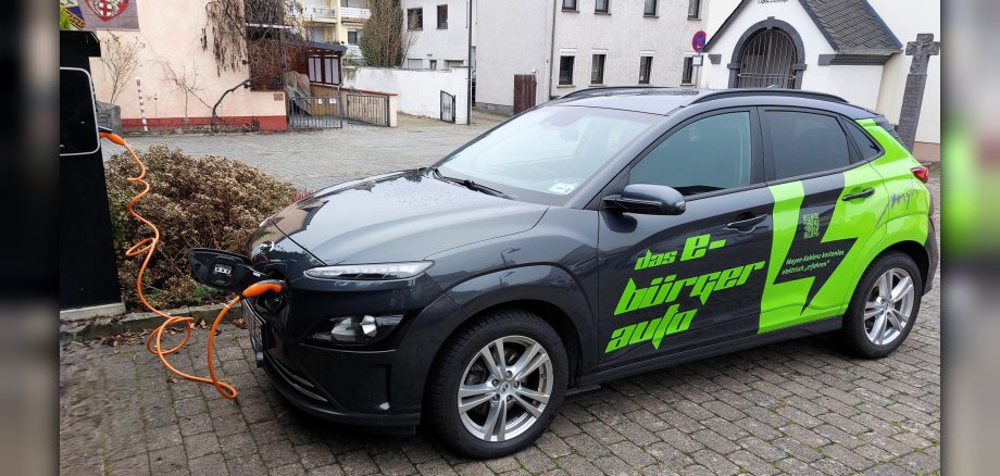 Das grün-schwarz lackierte Modell des E-Bürgerautos steht an einer Ladesäule und wird geladen. 