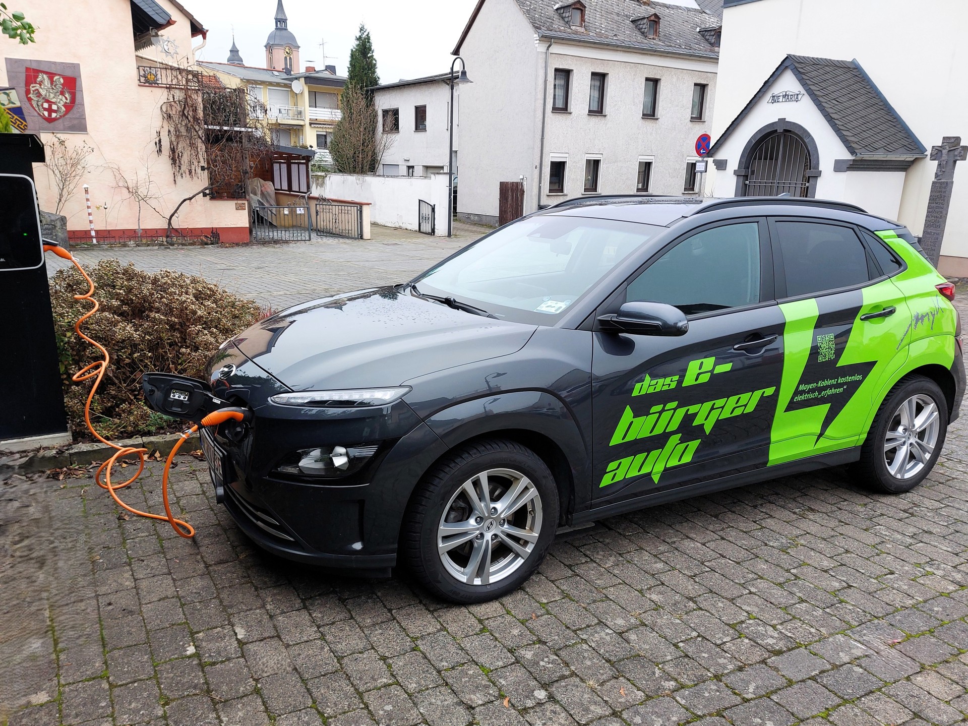 E-Bürgerauto Das grün-schwarz lackierte Modell des E-Bürgerautos steht an einer Ladesäule und wird geladen.