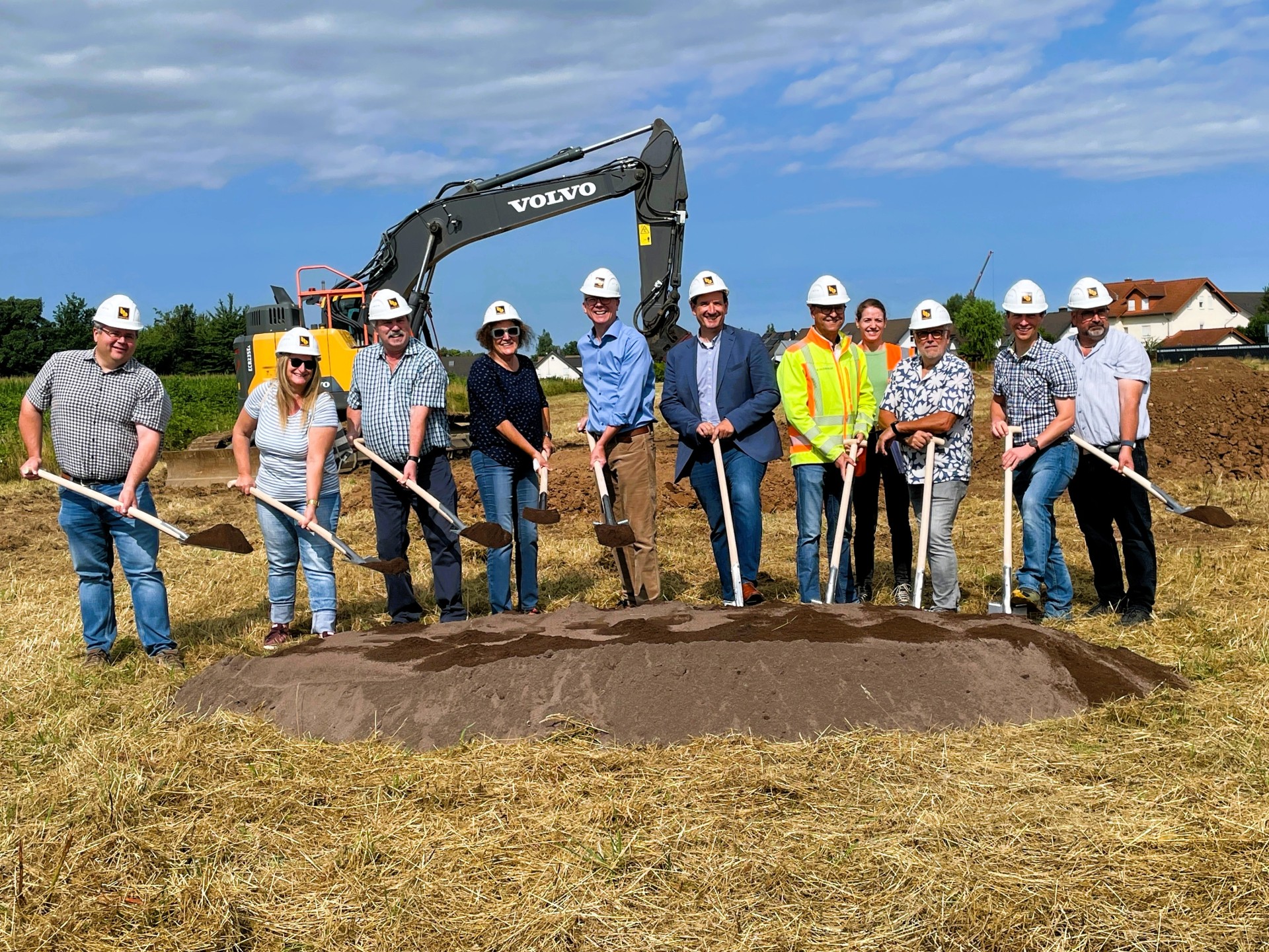 Ortsbürgermeister Norbert Bahl und VG-Bürgermeister Thomas Przybylla machen mit weiteren Vertretern der VG-Verwaltung, der Planungsbüros und der Baufirma den ersten Spatenstich mit Schaufeln und Helm auf dem Kopf. 