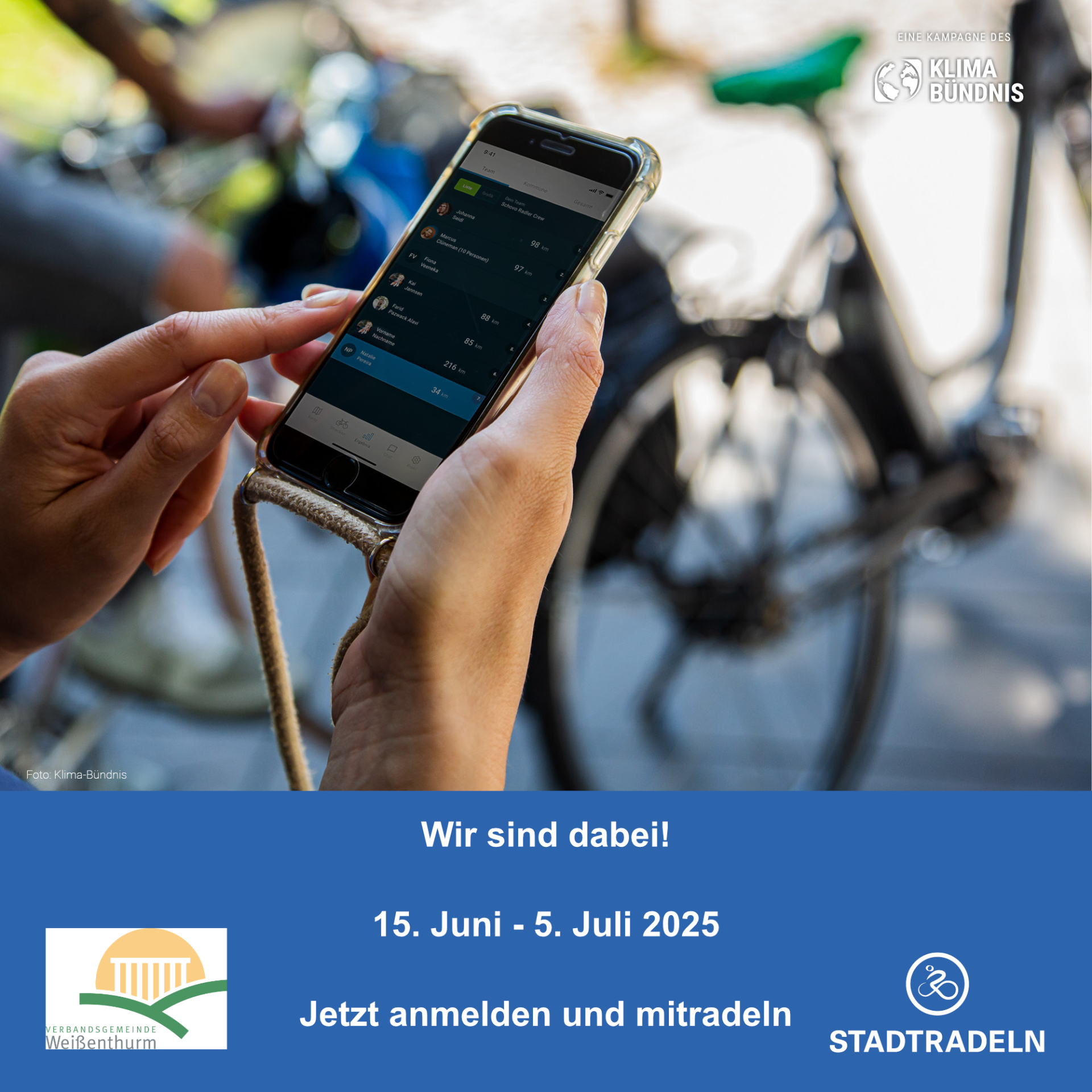 Stadtradeln Anmeldung Vor einem Fahrrad im Hintergrund hält eine Person in ihren beiden Händen ein Handy, auf dem die App zum Stadtradeln geöffnet ist.
