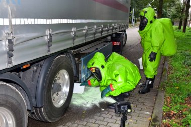 Feuerwehrübung Giftstoffeinsatz Zwei Feuerwehrleute in grünen Schutzanzügen sichern giftiges Material unter einem LKW.