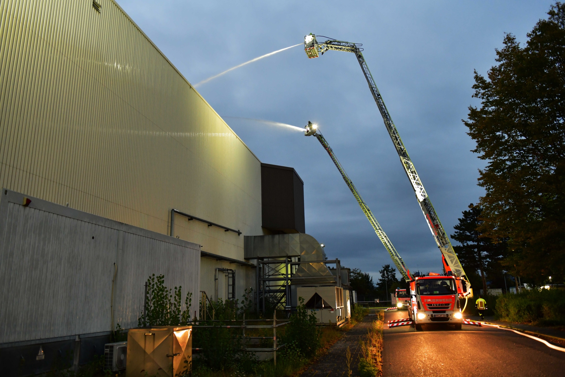 Feuerwehrübung Brand Zwei Löschfahrzeuge bekämpfen einen Brand an einer großen Halle.