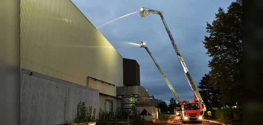 Zwei Löschfahrzeuge bekämpfen einen Brand an einer großen Halle.