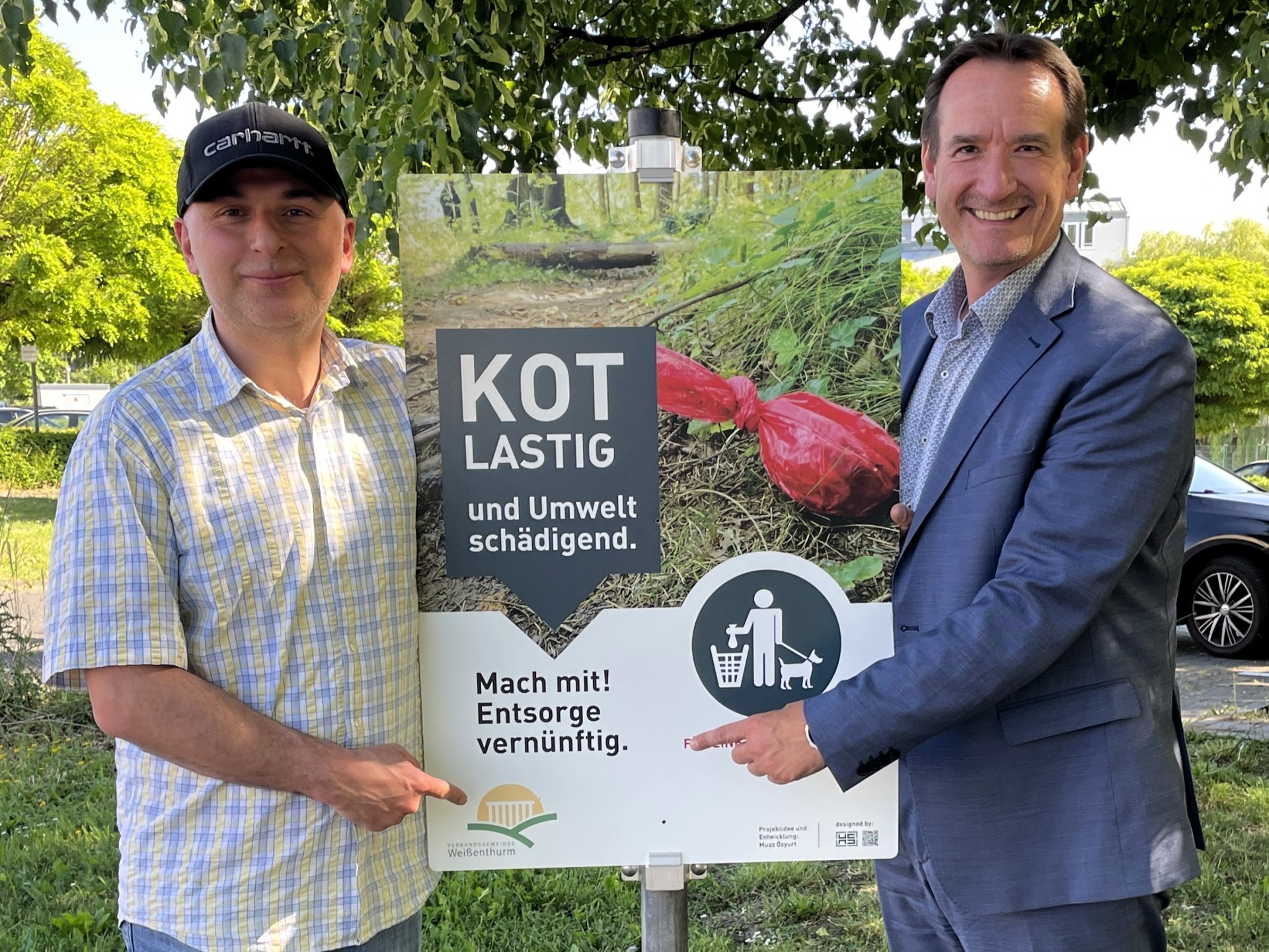 VG beteiligt sich an Anti-Müll-Kampagne Der Initiator der Kampagne, Mesut Özyurt, steht links des Schildes, das dazu aufruft, Hundekot nicht liegenzulassen. Rechts steht Bürgermeister Przybylla.