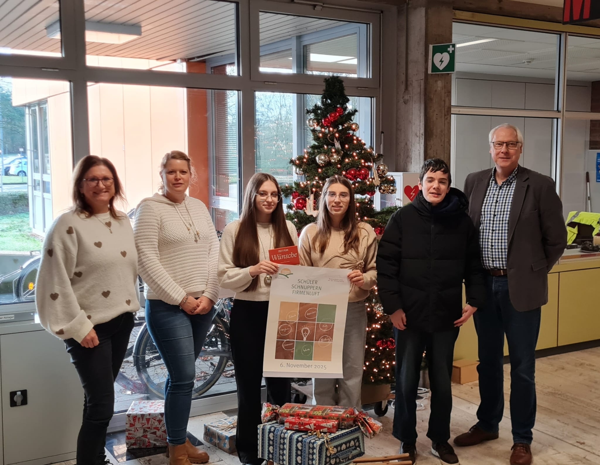Jobfüxin Katrtin Lyding, Projektbeauftragte Kristina Uerz und Schulleiter Gerhard Müller stehen mit den Schülerinnen und dem Schüler, die den Präsentationswettbewerb gewonnen haben, vor einem Weihnachtsbaum.