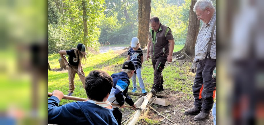 Unter Anleitung von Förster Dieter Kaul schälen Kinder im Wald die Rinde von einem Baumstamm. 