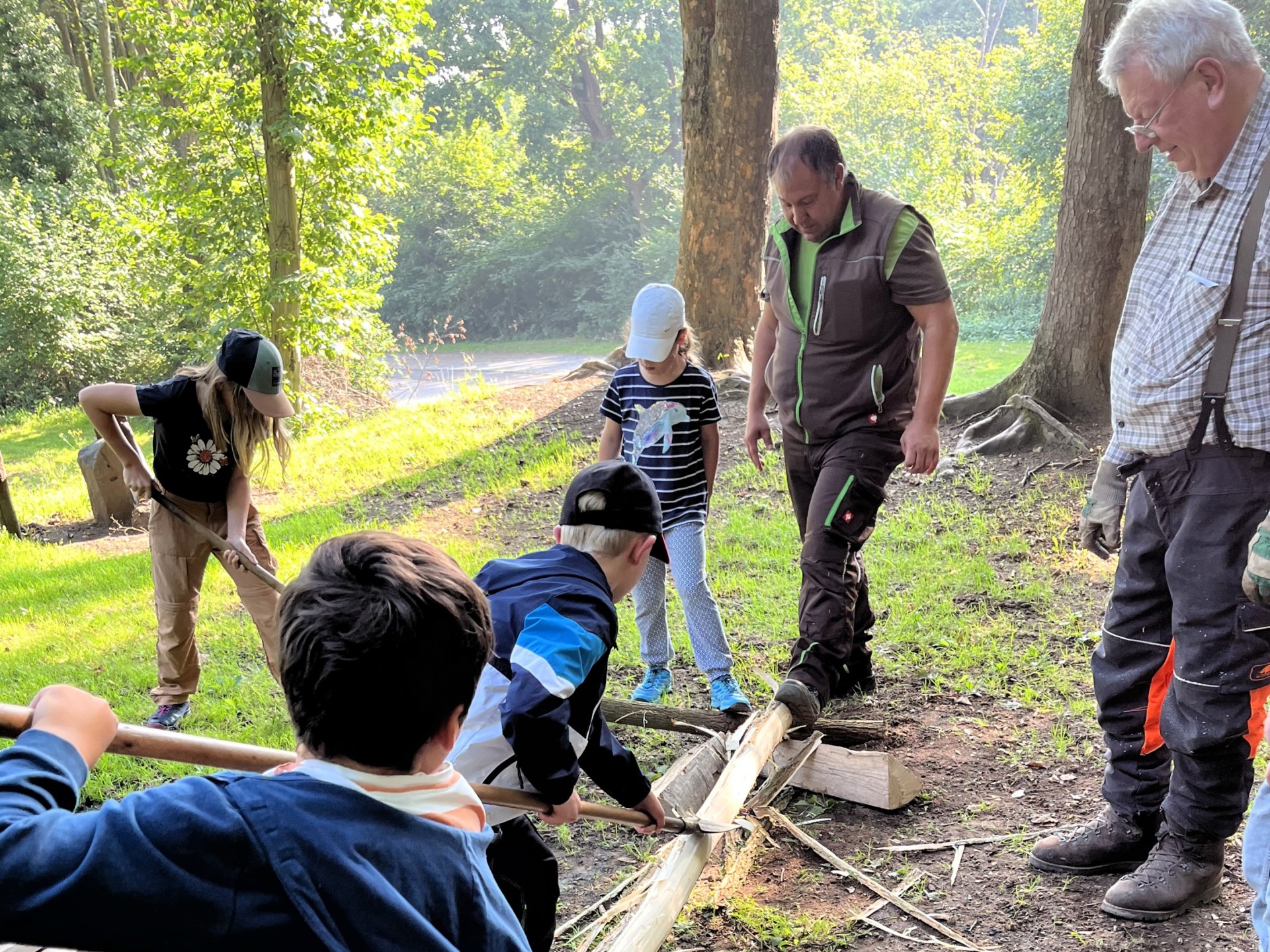 Waldaktivtag Rinde schälen Unter Anleitung von Förster Dieter Kaul schälen Kinder im Wald die Rinde von einem Baumstamm.