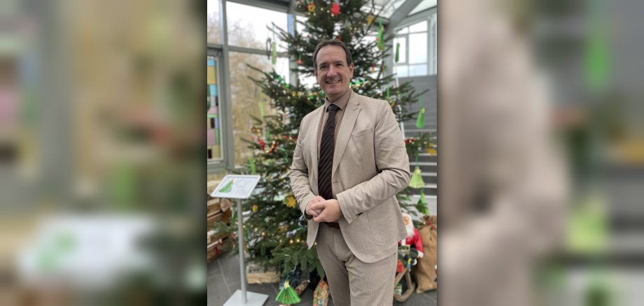 Bürgermeister Thomas Przybylla steht im Foyer des Rathauses vor dem geschmückten Weihnachtsbaum.
