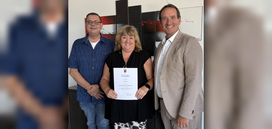 Dienstjubiläum Alexandra Gerhards Foto Alexandra Gerhards steht mit einer Dankurkunde zwischen Bürgermeister Thomas Przybylla und Personalratsvorsitzendem Marko Röser.