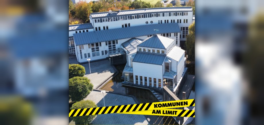Am unteren Bildrand ist über dem Rathaus der VG das gelb-schwarze Absperrband des Aktionstags mit dem Schriftzug "Kommunen am Limit" zu sehen. 