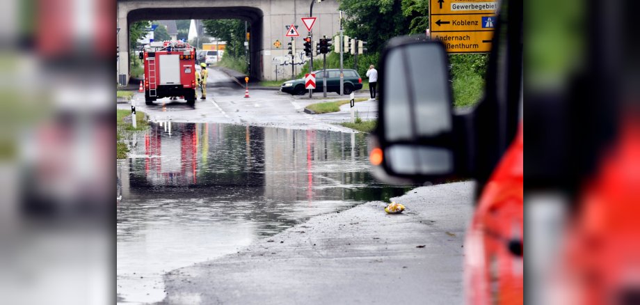 Foto Infoveranstaltung Hochwasserkonzept Eine überflutete Straße wird von Feuerwehrfahrzeugen bewacht.