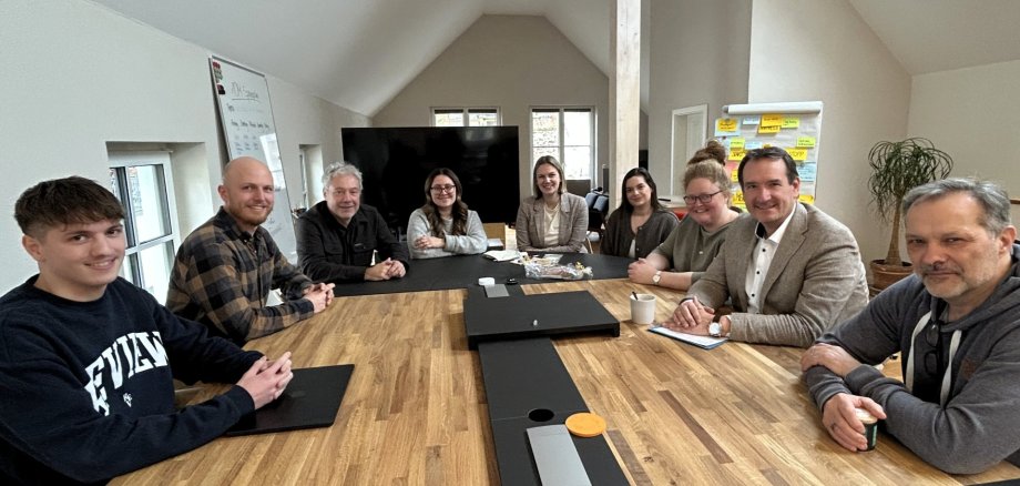 Um einen großen Tisch in den Büroräumen der 10M GmbH sitzen Mitarbeiterinnen und Mitarbeiter, VG-Bürgermeister Thomas Przybylla, VG-Mitarbeiterin Lena Rasch und Ortsbürgermeisterin Natalja Kronenberg. 