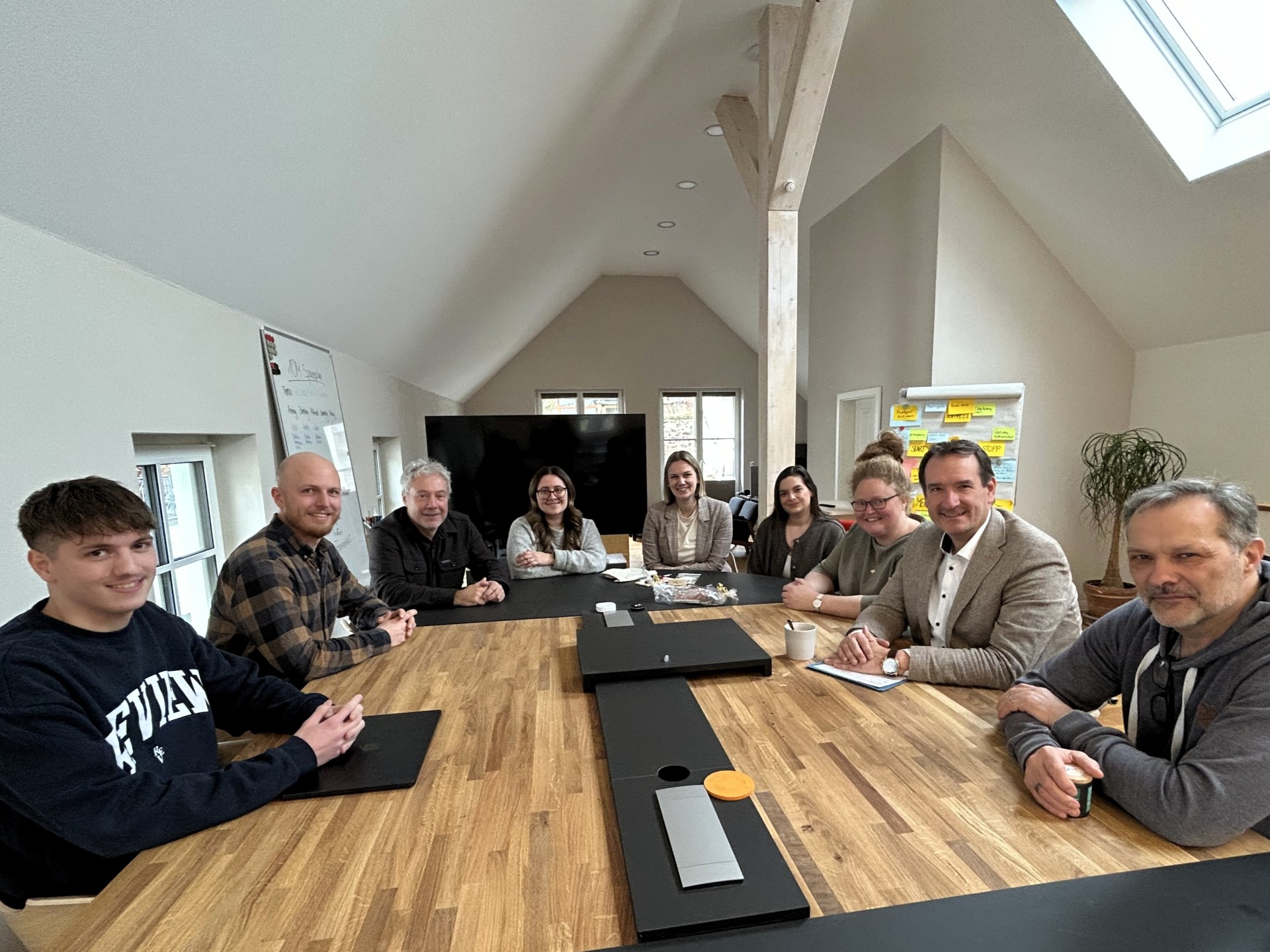 Besuch Verwaltung bei 10M Um einen großen Tisch in den Büroräumen der 10M GmbH sitzen Mitarbeiterinnen und Mitarbeiter, VG-Bürgermeister Thomas Przybylla, VG-Mitarbeiterin Lena Rasch und Ortsbürgermeisterin Natalja Kronenberg.