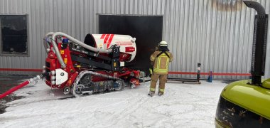 Hallenbrand Andernach Foto 3 Der Löschroboter steht mit einem Feuerwehrmann vor der Halle, an der Brandspuren erkennbar sind.