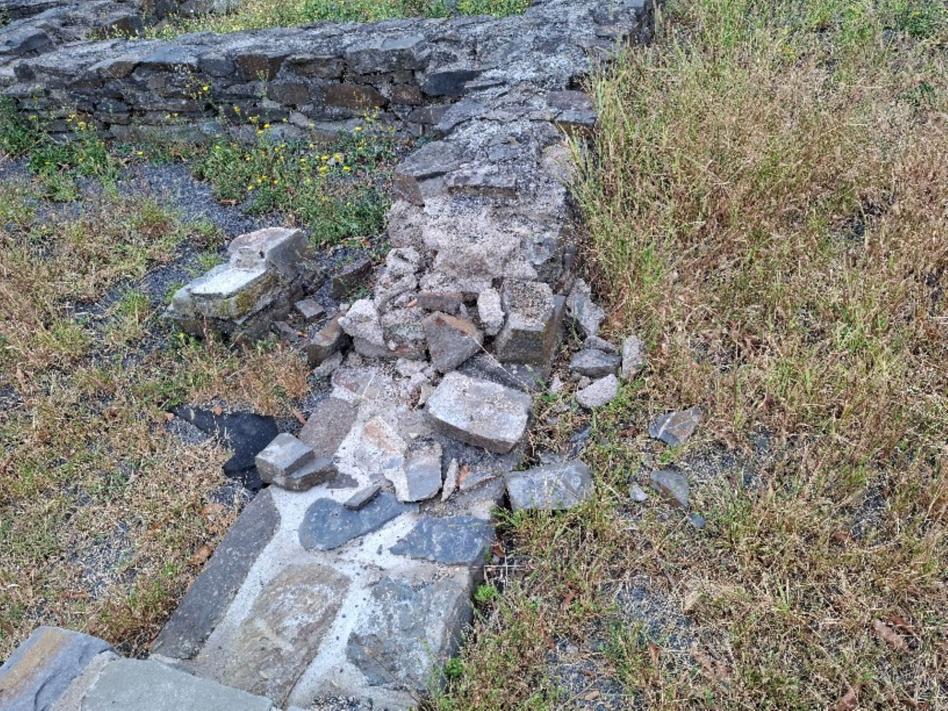 Eine zerstörte Mauer der Römervilla mit daneben liegenden Steinen.