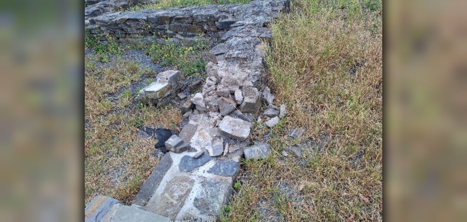 Vandalismus Römervilla Foto 1 Eine zerstörte Mauer der Römervilla mit daneben liegenden Steinen.