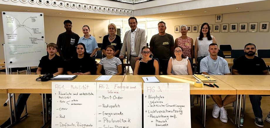 Azubi-Workshops Klimabeirat Die Azubis der VG sitzen im Ratssaal, dahinter stehen Bürgermeister Przybylla und drei Vertreter des Klimabeirats neben einem Flipchart mit Themen.