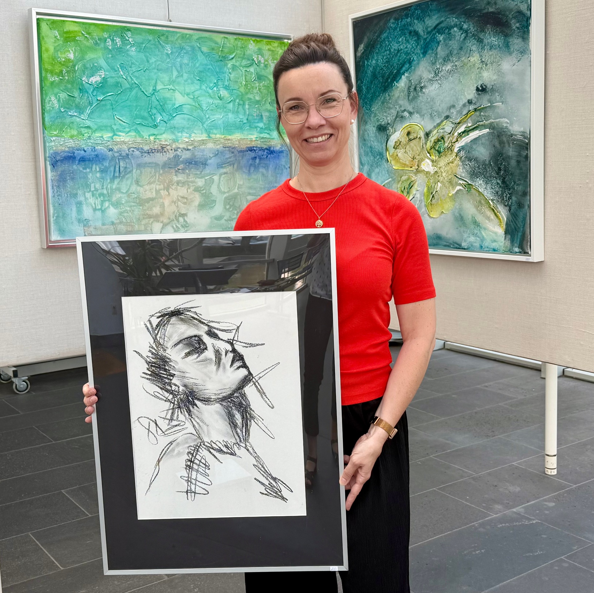 More than just colors“: Kunst im Foyer zeigt Werke, die Emotionen sichtbar machen Foto Künstlerin Miriam Lehnertz steht vor zwei Ausstellungswänden mit abstrakten Werken und hält eine gerahmte Skizze in den Händen.