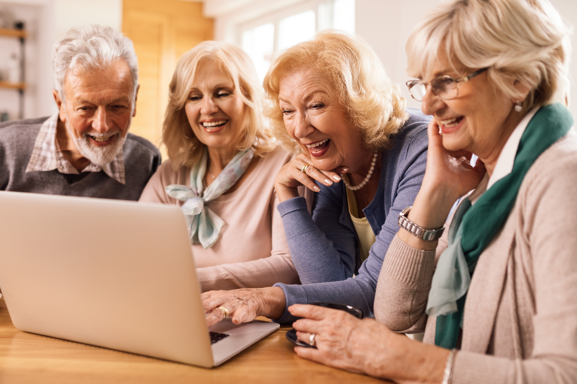 Drei ältere Frauen und ein älterer Mann sitzen vor einem aufgeklappten Laptop. 