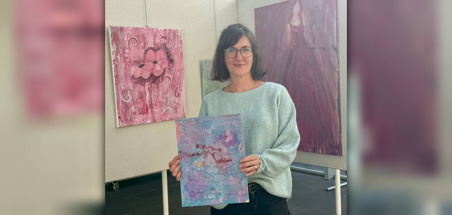 Ausstellung Poesie in Pastell Foto Die Künstlerin Annika Hill steht mit einem ihrer Bilder vor Ausstellungswänden mit ihren Werken im Foyer des VG-Rathauses.