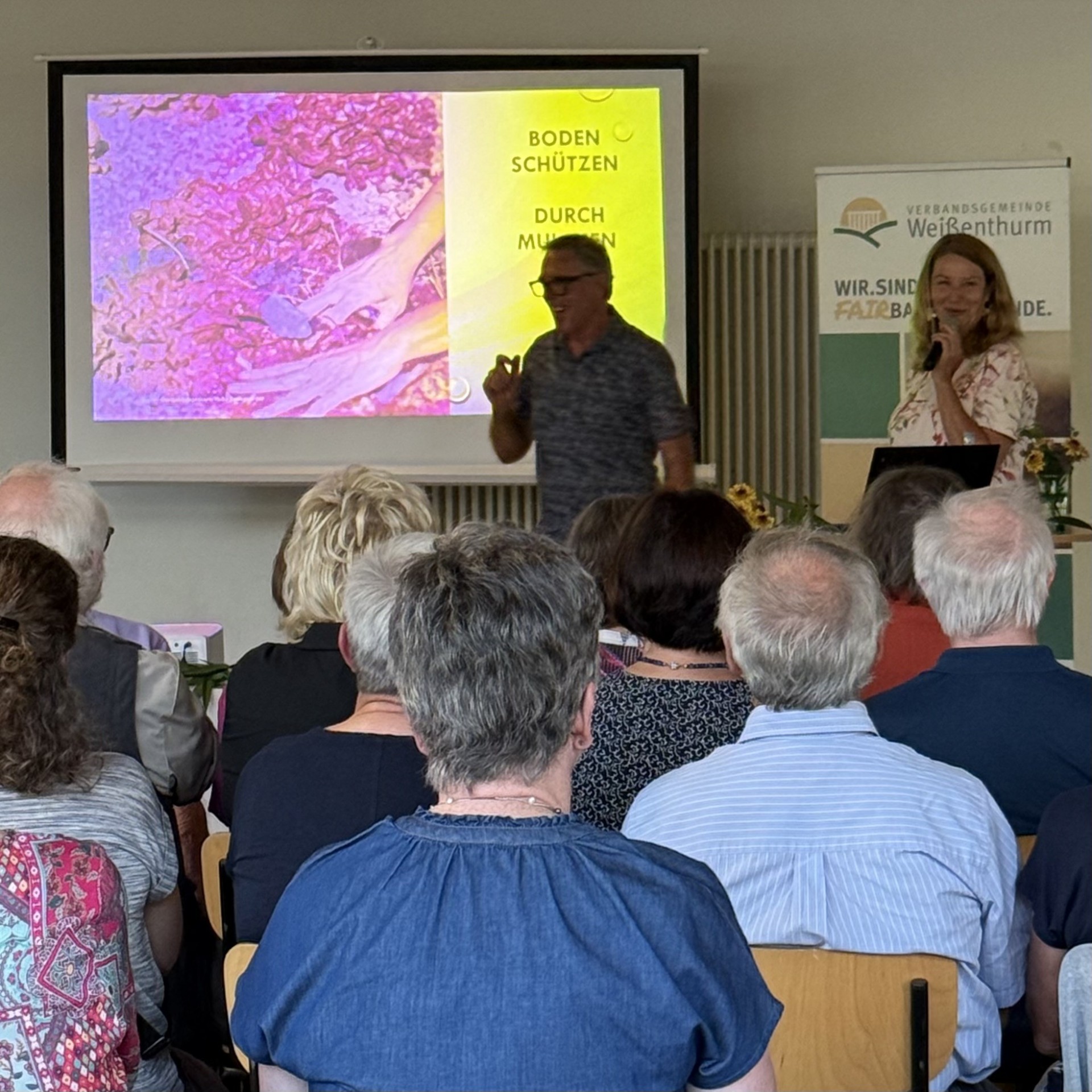 Vortrag Wasser pflanzen Foto Referenten Heike Boomgaarden und Werner Ollig stehen vor ihrer Präsentation, das Publikum sitzt mit dem Rücken zum Betrachter.