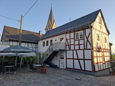 An der rückwärtigen Seite des Fachwerkhauses mit roten Balken ist ein Hof, in dem ein großer Sonnenschirm steht.
