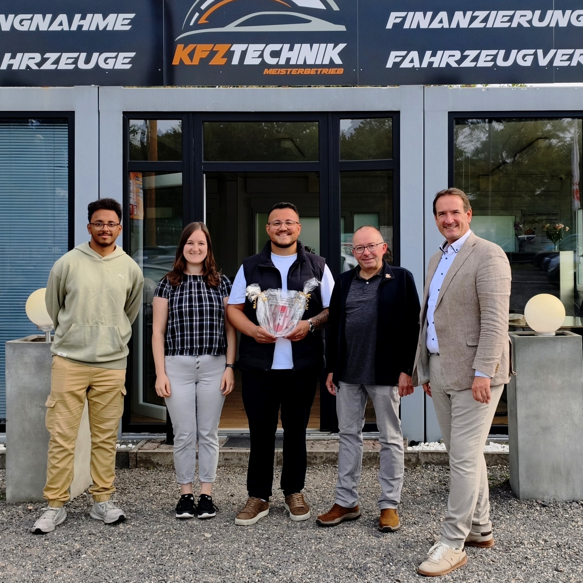 Besuch SMZ Foto VG-Bürgermeister Thomas Przybylla, Stadtbürgermeister Johannes Juchem, Unternehmer Dogukan Sarsilmaz, Wirtschaftsförderin Alina Kneip und ein Gast-Azubi stehen vor dem neu eröffneten Gebrauchtwagenhandel.