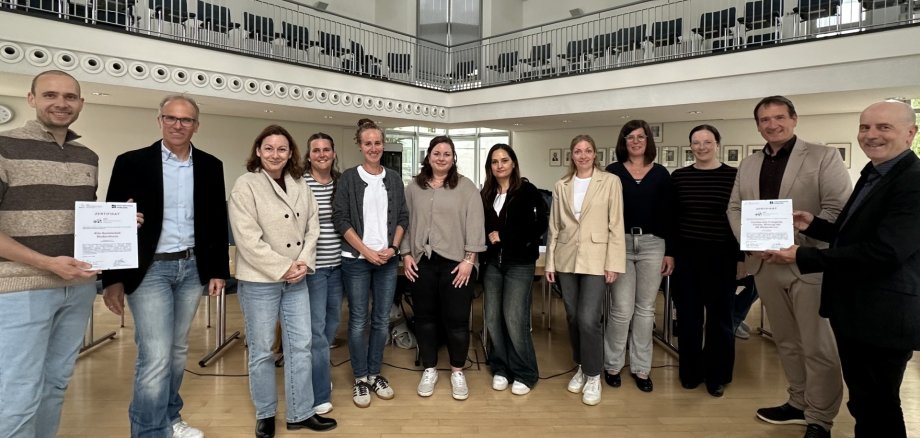 QID-Zertifikat Foto Alle am Prozess Beteiligten stehen mit Bürgermeister Thomas Przybylla und Fachbereichsleiter Sven Normann mit jeweils einer Urkunde im VG-Ratssaal.
